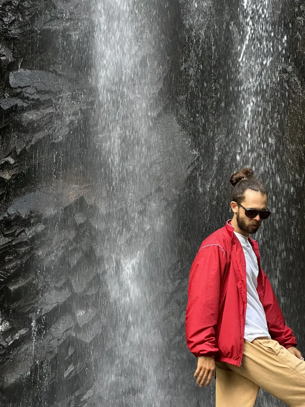 Portrait by a mountain waterfall, red jacket and sunglasses