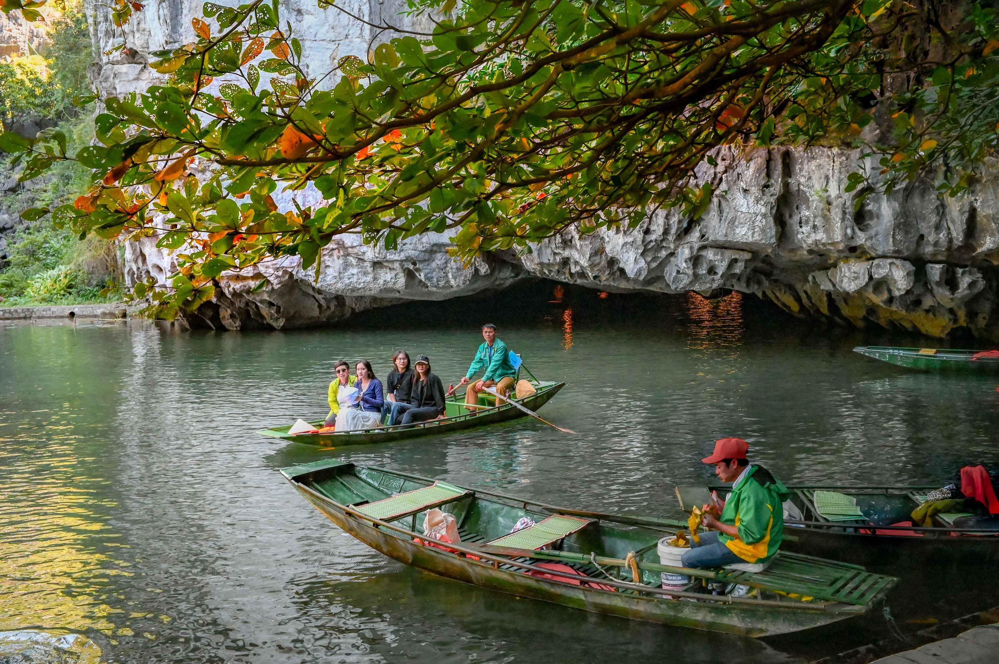 Rowboat carrying tourists through Trang An’s low limestone cave entrance