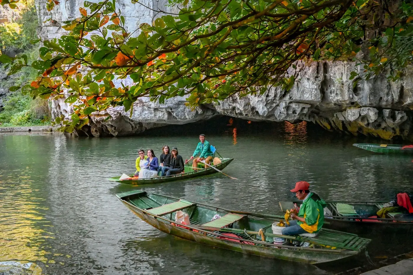 Rowboat carrying tourists through Trang An’s low limestone cave entrance