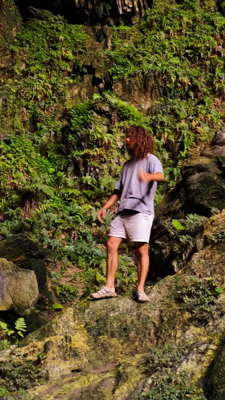 Traveler climbing moss-covered rocks inside a Ninh Binh cave