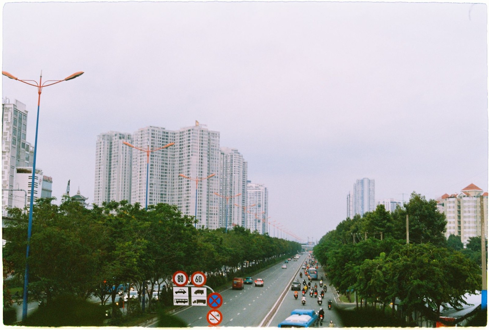 Vietnamese highway with speed limit signs and motorbike traffic near high-rise buildings