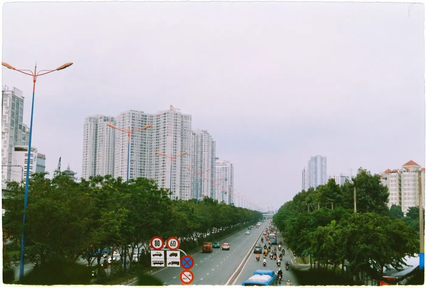 Vietnamese highway with speed limit signs and motorbike traffic near high-rise buildings