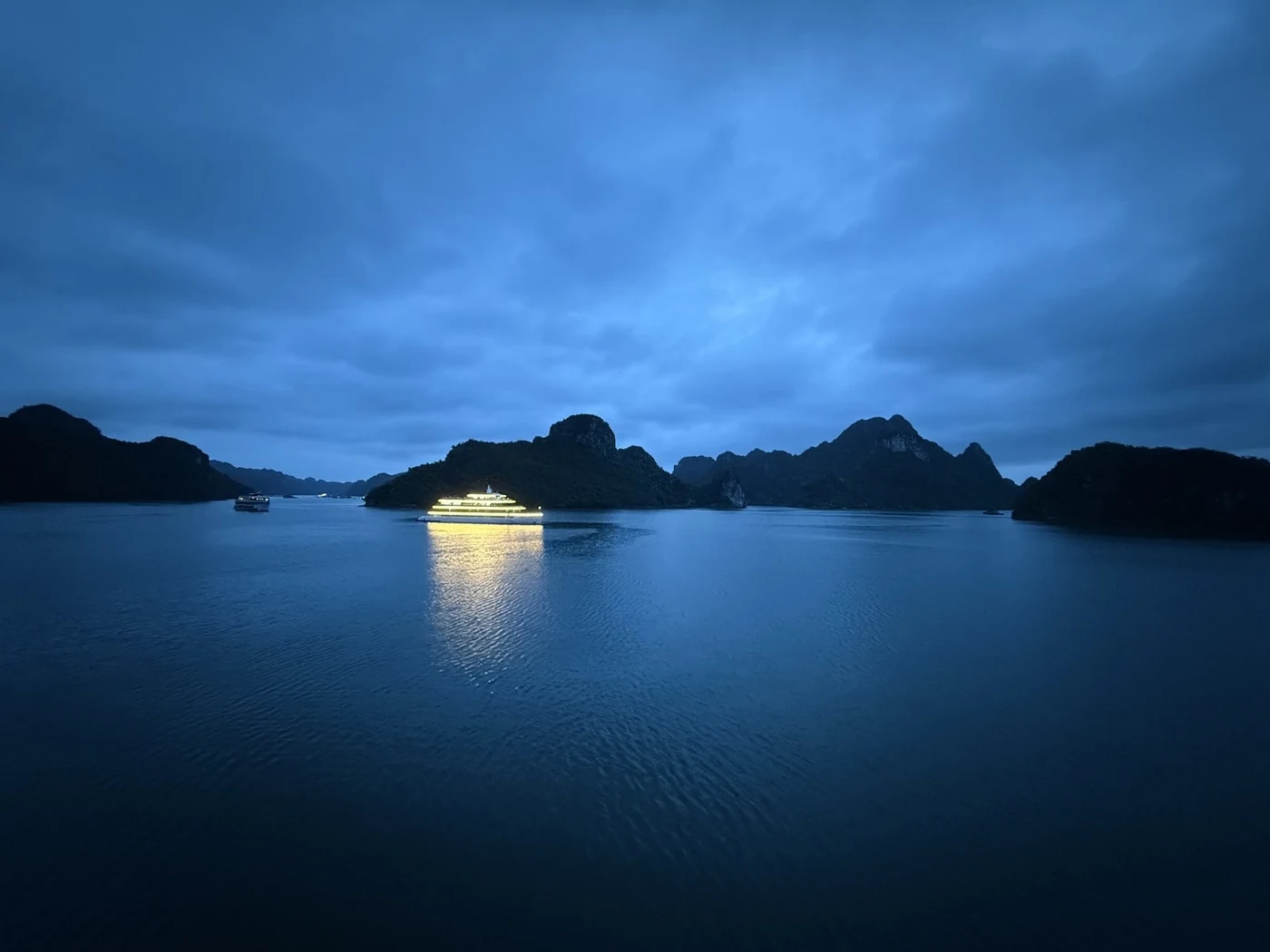 Illuminated ship between rock islands in Ha Long Bay in the evening