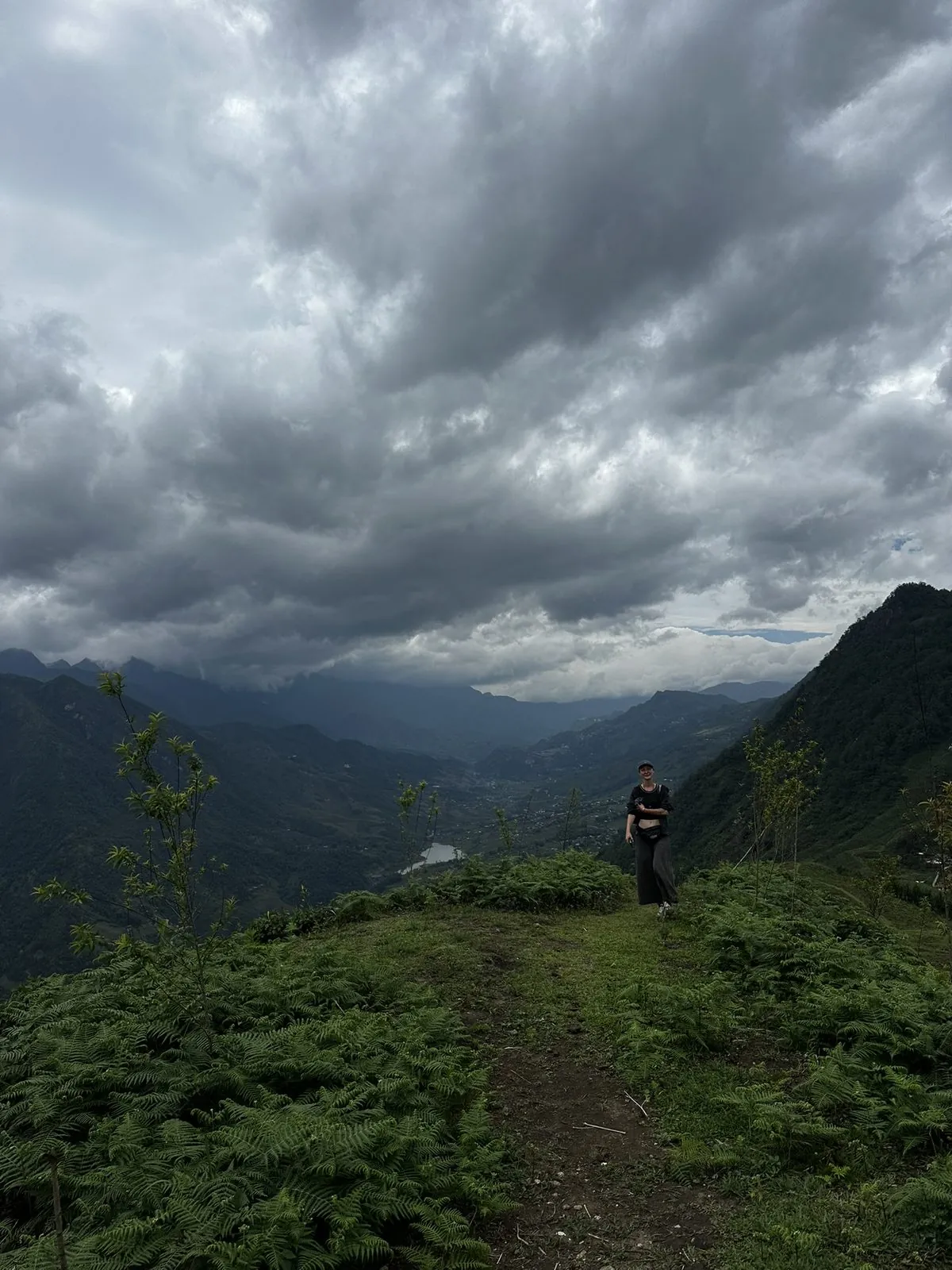 A lone figure on a mountain ridge under storm clouds above a valley in Sapa