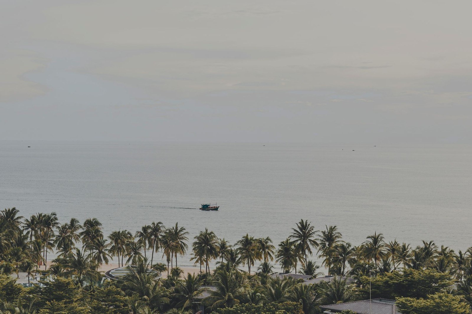 Palm trees along a quiet beach in Phu Quoc, Vietnam, with a fishing boat offshore