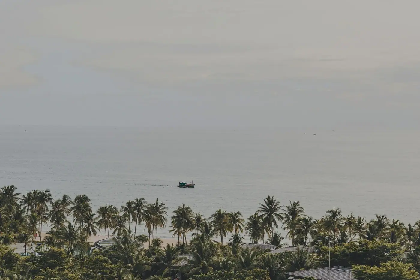 Palm trees along a quiet beach in Phu Quoc, Vietnam, with a fishing boat offshore