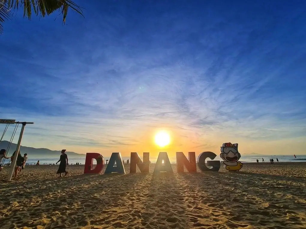 People walking on Da Nang beach at sunset next to a large DANANG sign