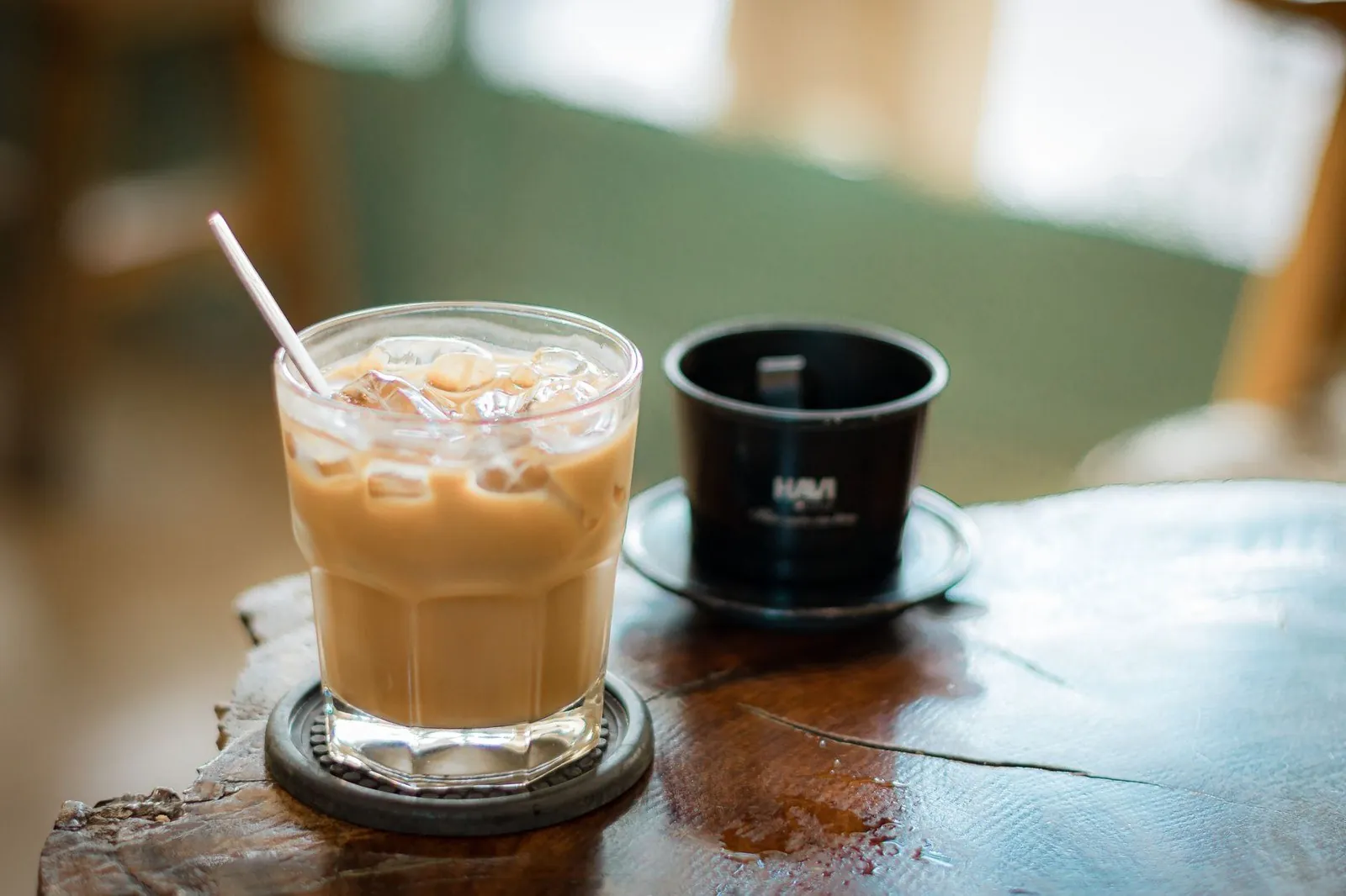 Iced Vietnamese coffee glass next to a dark phin brewing cup on a saucer
