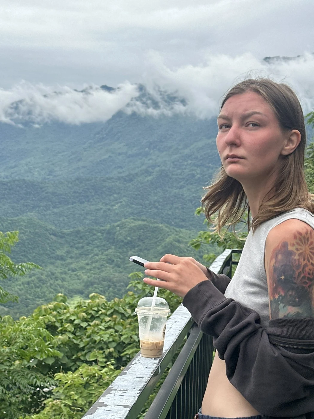 Iced coffee in a plastic cup on a mountain viewpoint railing with misty green hills