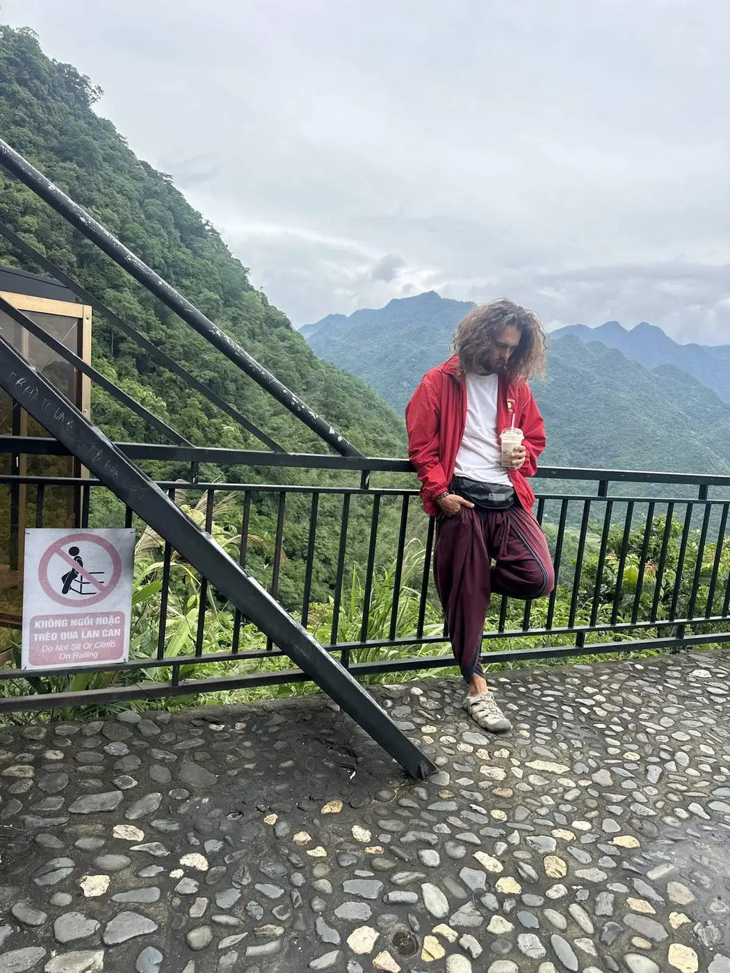 Traveller in a red jacket at the railing of a mountain coffee shop with misty jungle