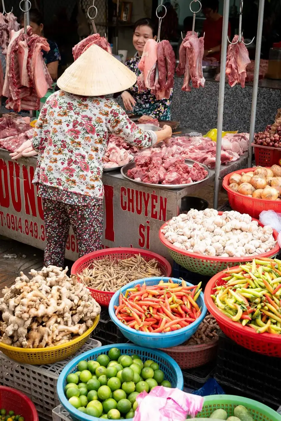 A vendor in a conical non la hat selects meat at a Da Nang wet market