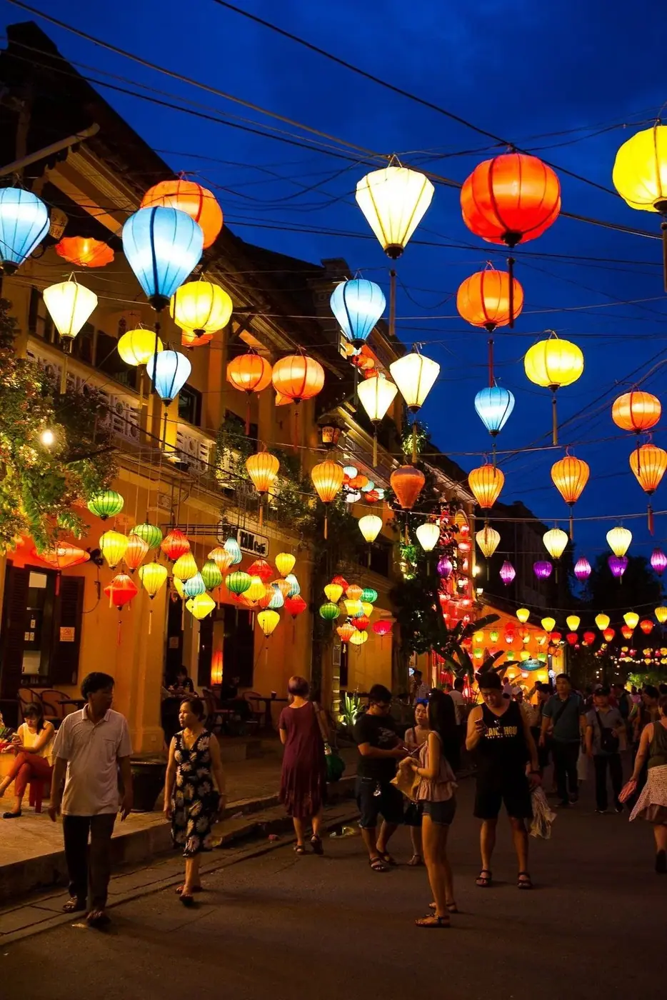 Tourists walking down Hoi An’s lantern-lit Old Town street at dusk