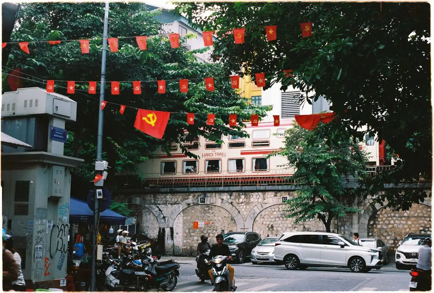 Stone railway arches behind a busy street hung with red flags in central Hanoi