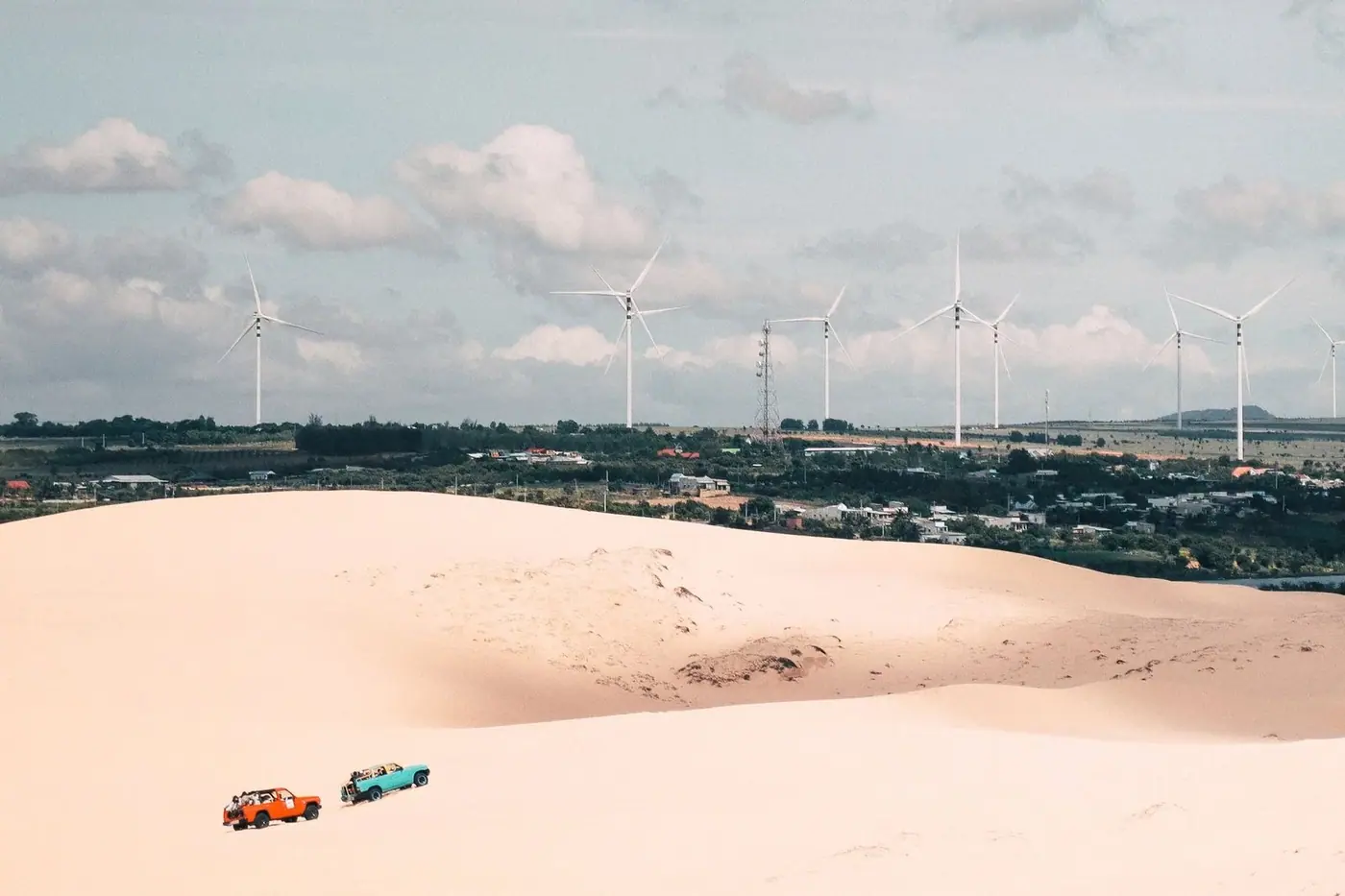 Sand dunes with wind turbines and off-road jeeps in the distance