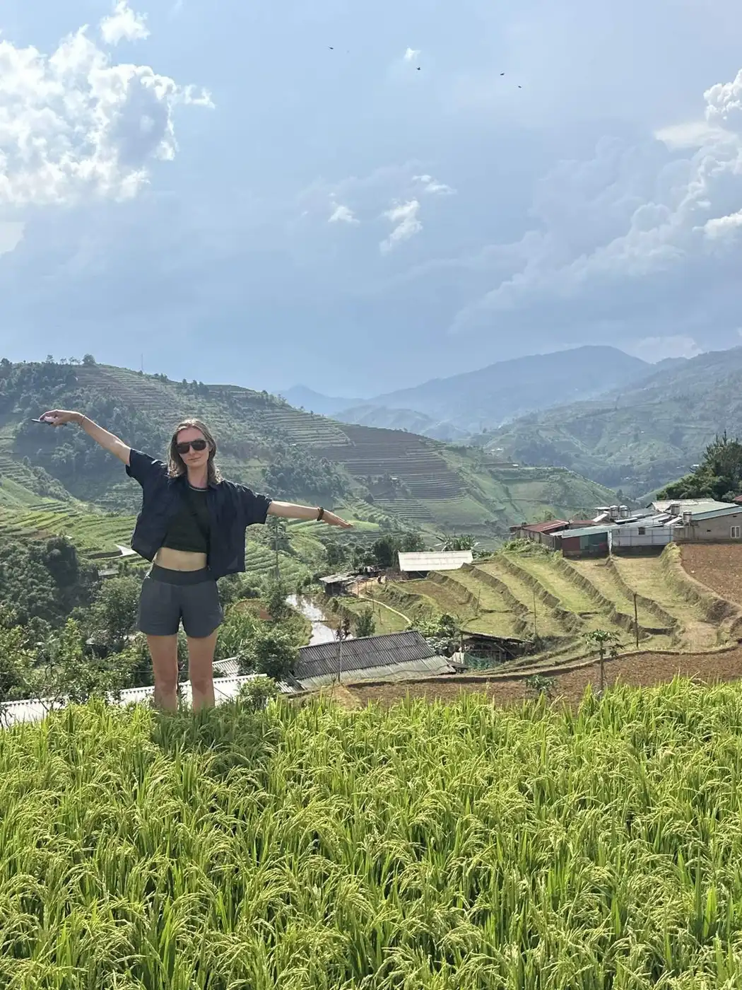 Traveller with arms outstretched above green rice terraces in a mountain valley near Sapa