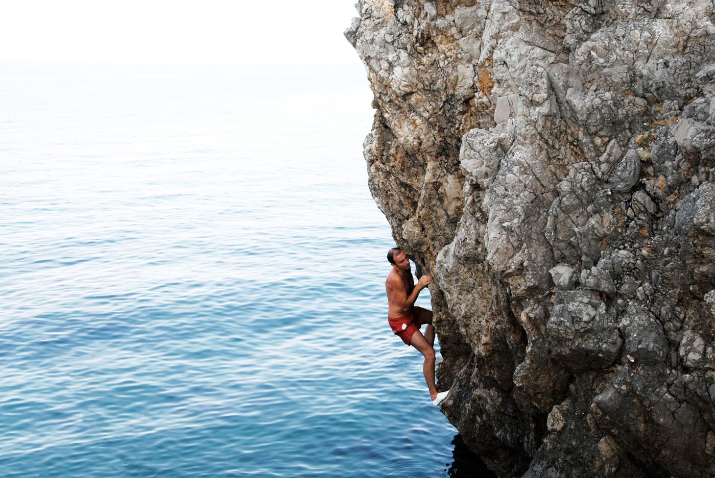Rock climber on limestone cliff above turquoise water